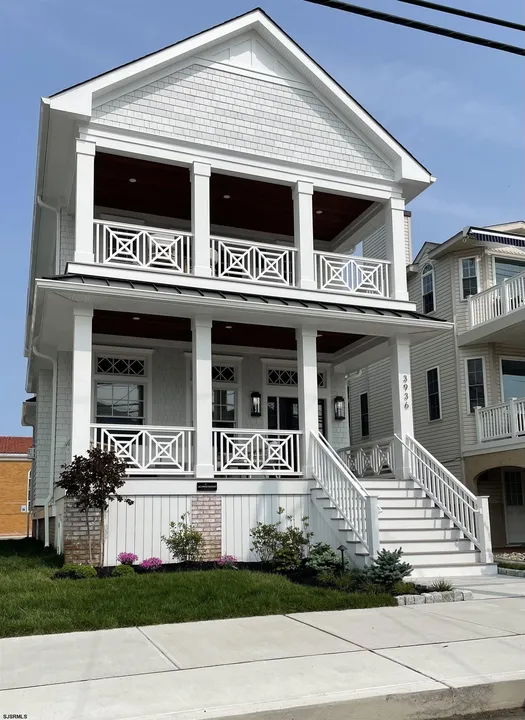 We see the front porch area of a large, tall, white house in Ocean City, NJ against a clear blue sky.