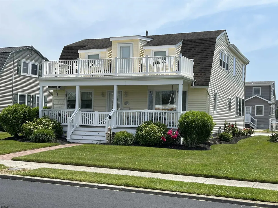 We see the front porch area of a beige house against a cloudy blue sky in Ocean City, NJ.