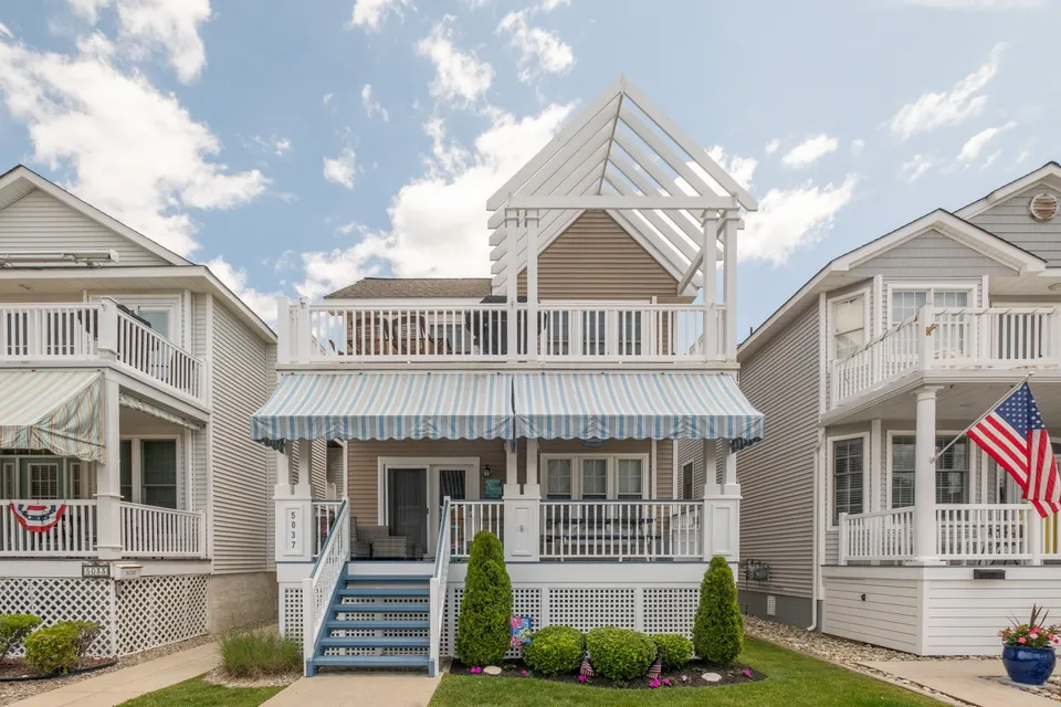 We see the front of a white and beige house in Ocean City, NJ against a cloudy blue sky.